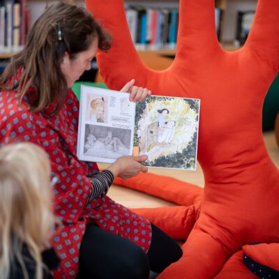 Image of a woman showing the a book to a few kids in the library in the Nordic House